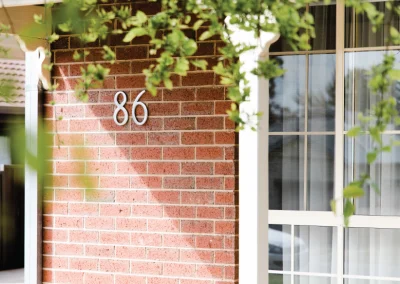 A house number 86 on a brick wall with sweeping vines falling into frame from the top